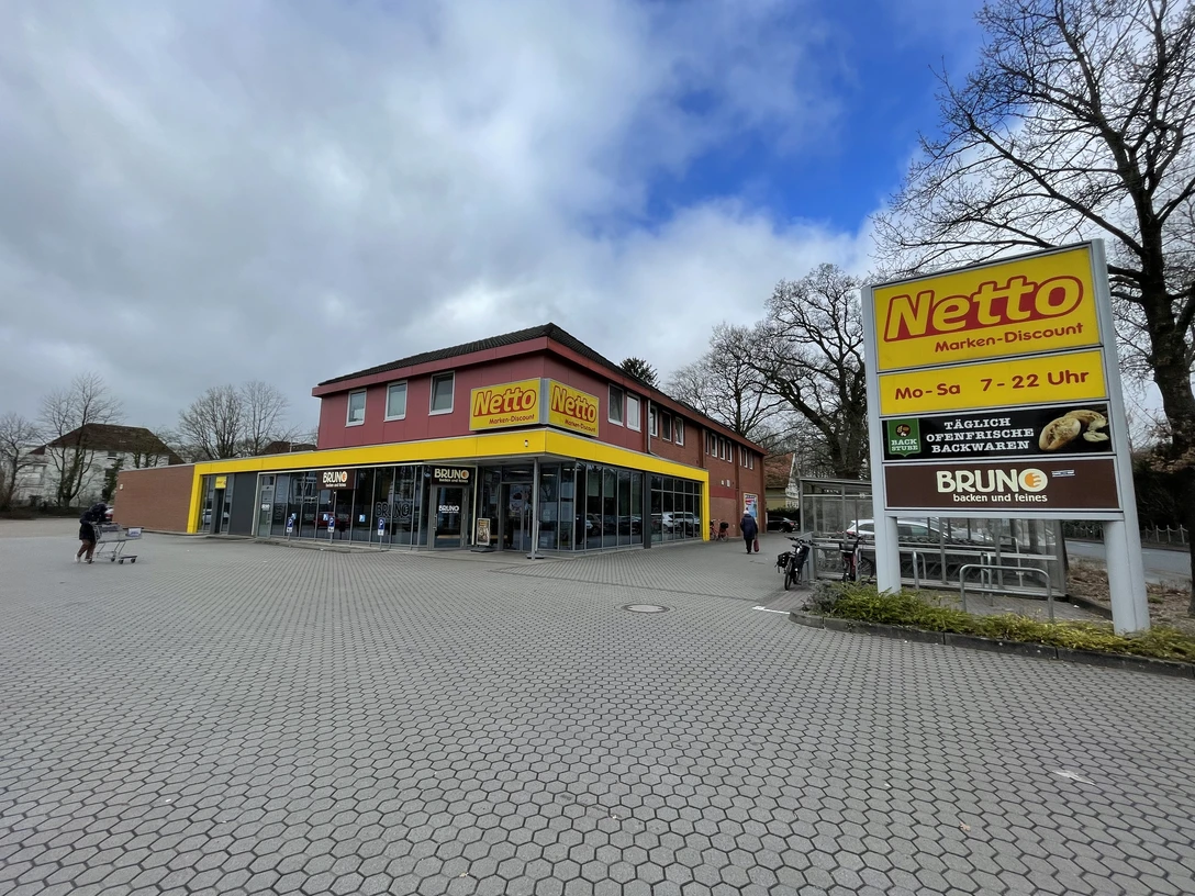 Netto Oldenburger Straße.jpg Das Bild zeigt einen Netto-Marken-Discount mit roter Fassade und gelbem Logo, eingerahmt von Bäumen.