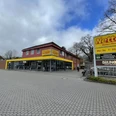 Netto Oldenburger Straße.jpg Das Bild zeigt einen Netto-Marken-Discount mit roter Fassade und gelbem Logo, eingerahmt von Bäumen.