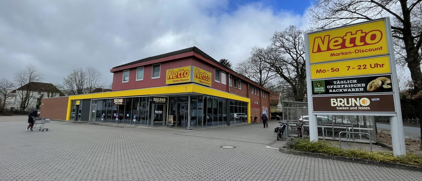 Netto Oldenburger Straße.jpg Das Bild zeigt einen Netto-Marken-Discount mit roter Fassade und gelbem Logo, eingerahmt von Bäumen.