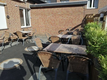 Sonniger Außenbereich eines Imbisses mit mehreren leeren Tischen und Stühlen auf einer gepflasterten Terrasse.