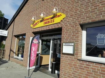 Enders Fleischerimbiss_Pro Herford (1).jpg Enders Fleischerimbiss mit offenem Eingang, drei Fassadenlampen und einer Coffeefair-Flagge außen.