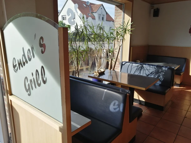 Enders Fleischerimbiss_Pro Herford (3).jpg Ein heller Imbiss mit Holzinterieur und Pflanzen, einladender Sitzbereich und Glaswände für viel Licht.