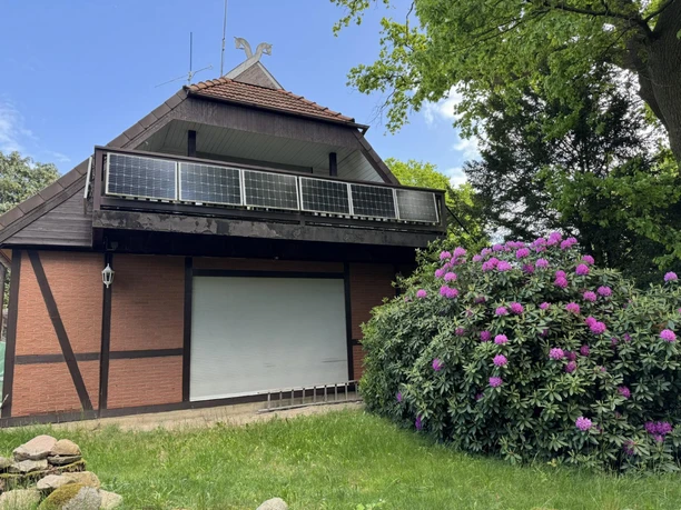 ferienwohnung-alscher-amelinghausen-solarbalkon-rhododendron.JPG Du siehst eine malerische, rustikale Unterkunft mit einem charmanten Reetdach. Davor blüht ein prächtiger Rhododendron.