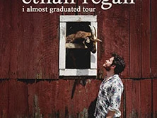 Ein Mann steht vor einer Holzwand mit Fenster, aus dem eine Ziege herausschaut. Oben Text mit "Ethan Regan".