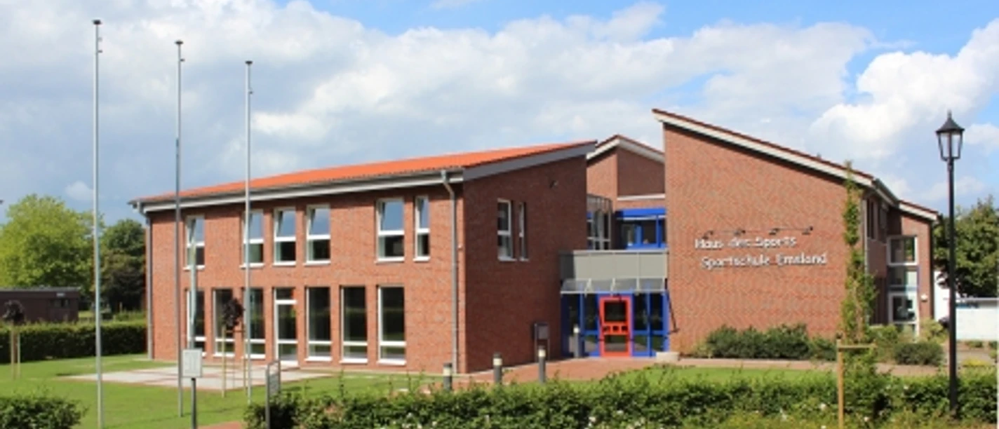 Haus_des_Sports.jpg Modernes Backsteingebäude mit rotem Dach, klaren Linien und gepflegtem Grün vor dem Eingang.