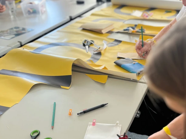 re:create Workshop <p>Menschen basteln an einem Tisch mit buntem Papier und Werkzeugen in einer hellen Umgebung.</p>