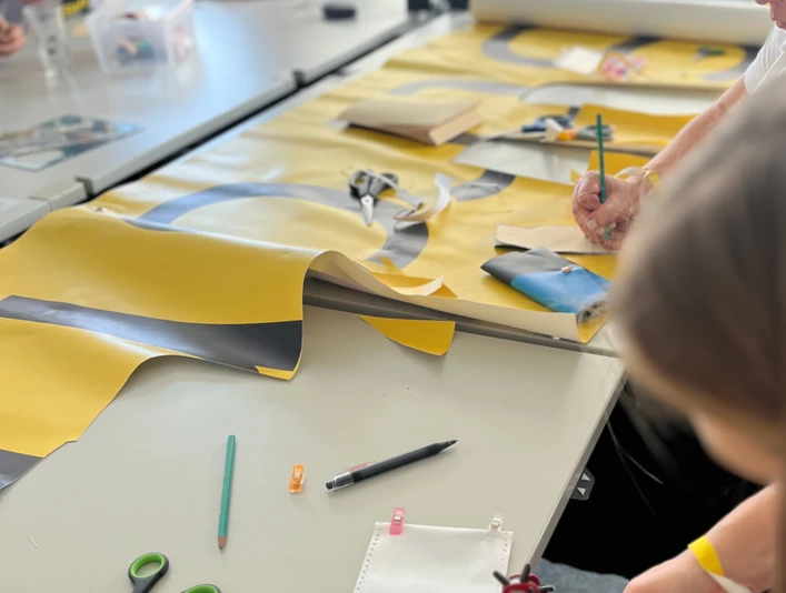 re:create Workshop <p>Menschen basteln an einem Tisch mit buntem Papier und Werkzeugen in einer hellen Umgebung.</p>