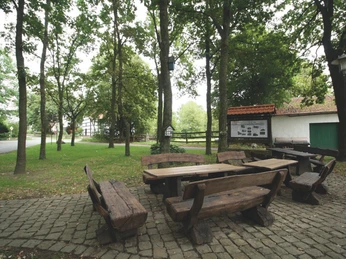 Dorfplatz Frotheim Holztisch mit Bänken auf gepflastertem Platz, umgeben von Bäumen und rustikalen Gebäuden.