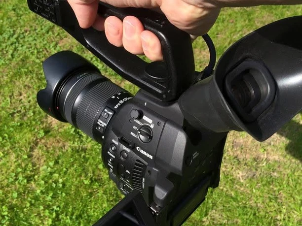 Jo Jonietz Ein Hand hält eine professionelle Videokamera über einer grünen Wiese.