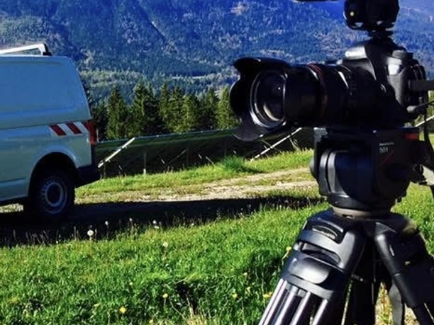 Bergmassiv Kamera auf Stativ vor Berglandschaft, daneben ein weißer Transporter.