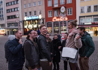 A cheerful group smiles as they explore Cologne's old town, surrounded by historic buildings and typical Cologne breweries.