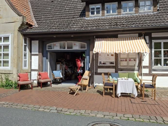 Café La Vie En Rose Ein malerisches Café mit farbenfroher Möblierung und gestreifter Markise an einem Fachwerkgebäude.