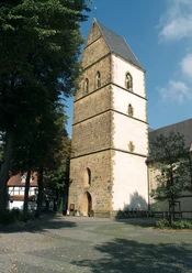 kirche.jpg Ein historischer Kirchturm aus Sandstein, umgeben von Bäumen, vor einem blauem Himmel.