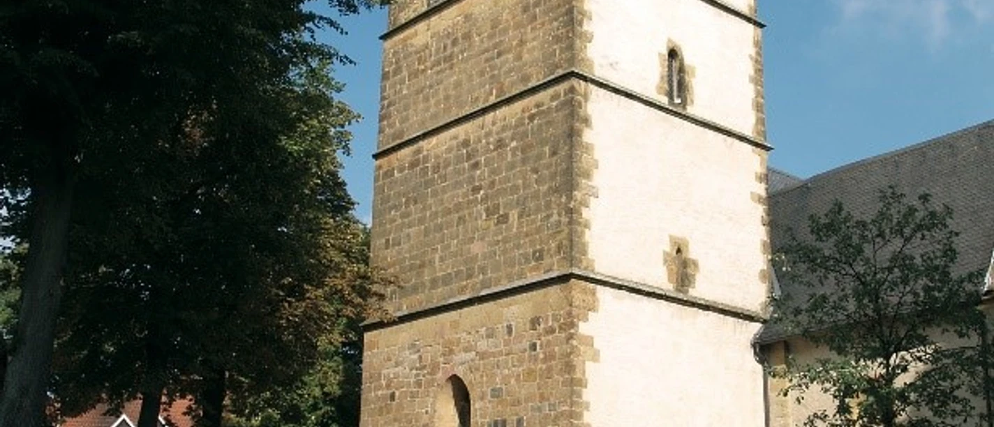 kirche.jpg Ein historischer Kirchturm aus Sandstein, umgeben von Bäumen, vor einem blauem Himmel.