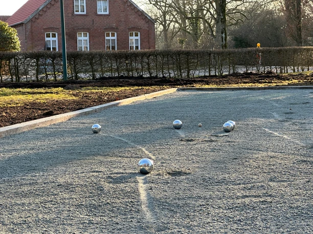 Bouleplatz in Backemoor, Gemeinde Rhauderfehn, Ostfriesland image0.jpeg Bouleplatz in Backemoor mit mehreren Metallkugeln auf dem Spielfeld vor einem Backsteinhaus und Hecke im Hintergrund
