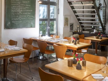 Christoph Pauls Restaurant Innenansicht eines stilvollen Restaurants mit Holztischen, modernen Stühlen und einer kunstvollen Dekoration.Interior view of a stylish restaurant with wooden tables, modern chairs, and artistic decor.