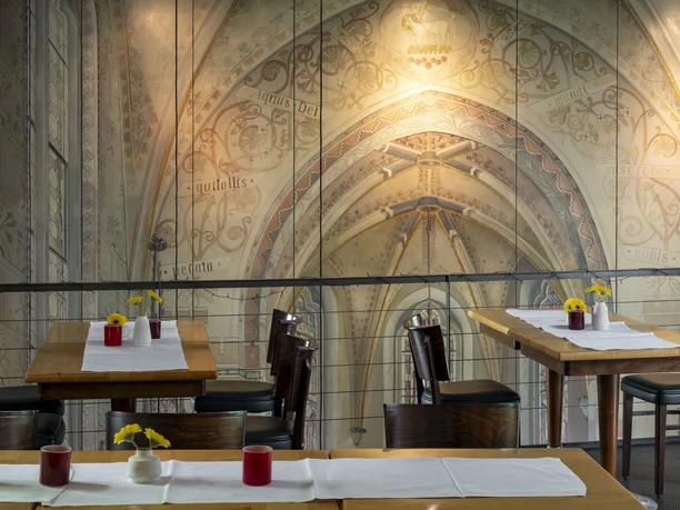 Christoph Pauls Restaurant A harmoniously designed restaurant area featuring elegantly arranged tables set against an artistically painted vaulted wall. The refined interior invites guests to linger, while small floral arrangements enhance the ambiance.