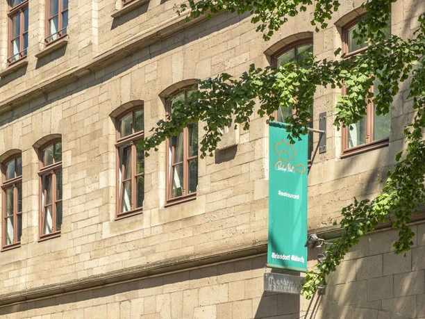 Christoph Pauls Restaurant View of a building with yellow brick walls, a green flag of Christoph Paul's restaurant, and large windows.