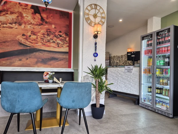 Innenansicht Pizzaria La Rosa Innenansicht einer modernen Gaststätte mit blau gepolsterten Stühlen an einem Tisch und einem Kühlschrank mit Getränken.