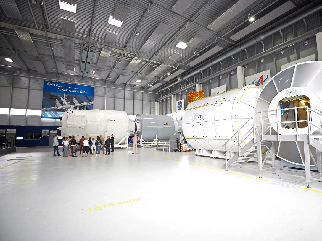 Deutsches-Zentrum-fuer-Luft-und-Raumfahrt-Gruppe-Axel-Schulten-KoelnTourismus-GmbH.jpg Innenansicht des Deutschen Zentrums für Luft- und Raumfahrt. Im Vordergrund ist eine Gruppe von Personen, die eine Führung durch eine große Halle erhalten, in der verschiedene Raumfahrmodule und technische Einrichtungen zu sehen sind.Interior view of the German Aerospace Center. In the foreground is a group of people being given a guided tour of a large hall in which various space modules and technical equipment can be seen.