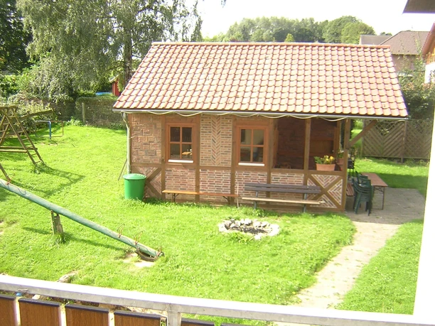Spielplatz mit Gartenhütte - Bauernhof-Pension Wüllner Braunes Gartenhaus mit Holzfenstern, Kinderspielplatz und Rasenfläche, im Hintergrund Bäume