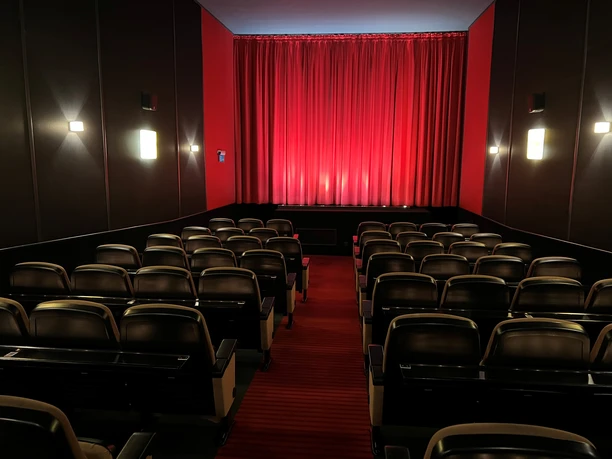 Filmhof Hoya Ein kleiner, intimer Kinosaal mit roten Wänden und Vorhängen. Reihen schwarzer Kinosessel stehen bereit.