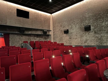 Filmhof Hoya Kinosaal mit roten Sitzreihen, gedämmter Beleuchtung und geschlossener Leinwand in ruhiger Atmosphäre.