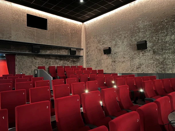 Filmhof Hoya Kinosaal mit roten Sitzreihen, gedämmter Beleuchtung und geschlossener Leinwand in ruhiger Atmosphäre.