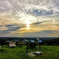 panorama_grosser_berg.jpg Sonnenuntergang über einer grünen Landschaft mit Info-Tafeln und Parkbänken unter dramatischem Himmel.