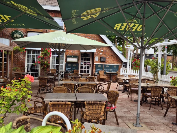 Außenansicht Restaurant Arkadia Gemütlicher Biergarten mit grünen Sonnenschirmen und Korbmöbeln, umgeben von Blumen und Bäumen.