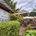 Außenansicht Restaurant Arkadia Gemütliche Außenterrasse des Restaurants Arkadia in idyllischer Gartenumgebung mit Sonnenschirmen und blühenden Pflanzen.