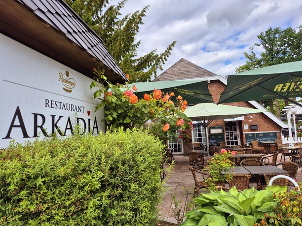Außenansicht Restaurant Arkadia Gemütliche Außenterrasse des Restaurants Arkadia in idyllischer Gartenumgebung mit Sonnenschirmen und blühenden Pflanzen.