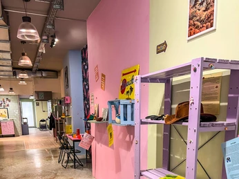 Museum des Schmerzes und der Liebe Ein einladender Raum mit pastellfarbenen Wänden, dekorativem Regal und Kunstwerken unter lebendigen Farbakzenten.A welcoming room featuring pastel-colored walls, a decorative shelf, and artworks accented by vibrant splashes of color.