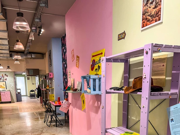 Museum des Schmerzes und der Liebe Ein einladender Raum mit pastellfarbenen Wänden, dekorativem Regal und Kunstwerken unter lebendigen Farbakzenten.