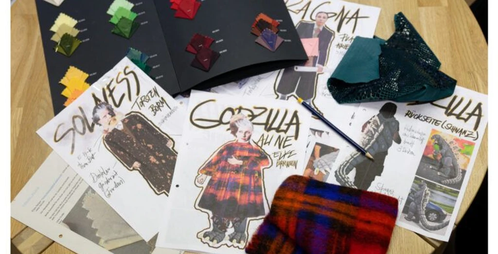 Designentwürfe und Stoffmuster für Theaterkostüme auf einem Holztisch.