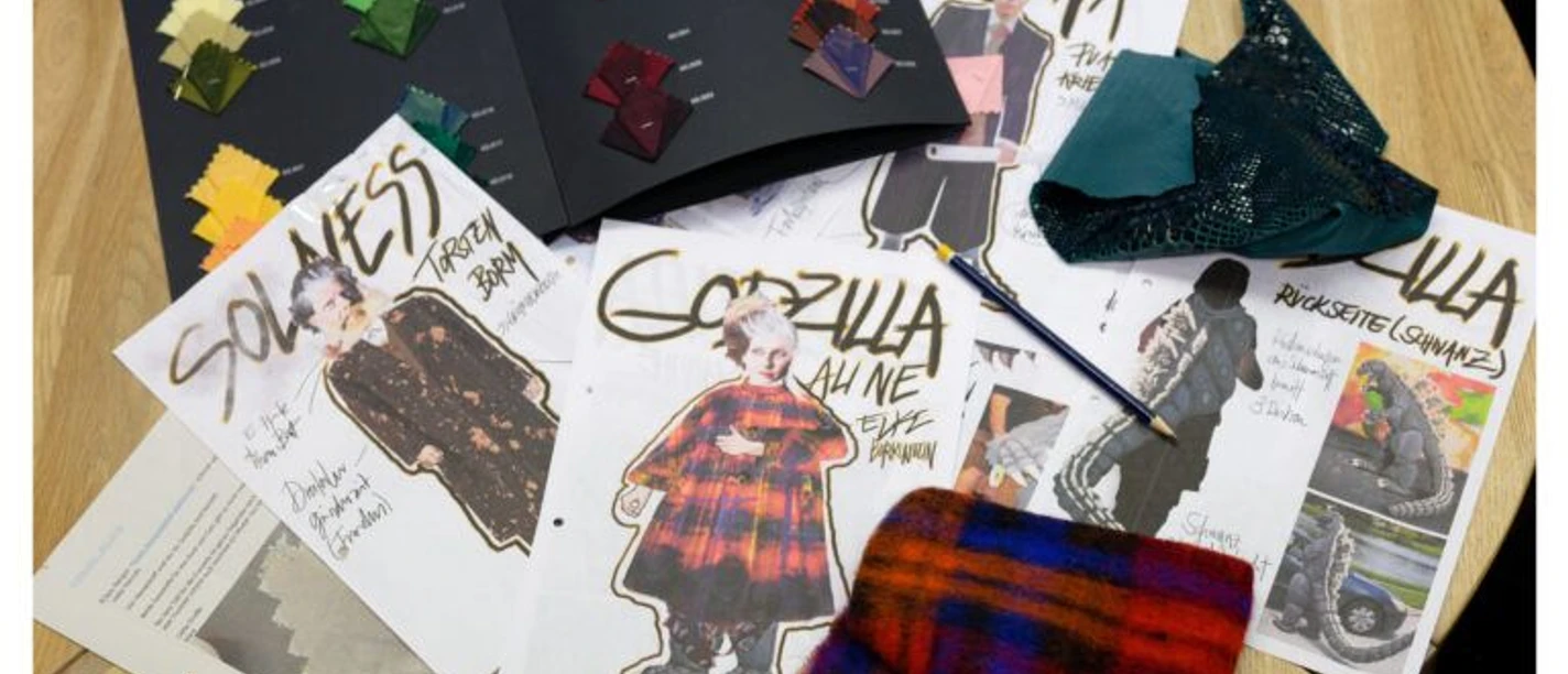 Designentwürfe und Stoffmuster für Theaterkostüme auf einem Holztisch.