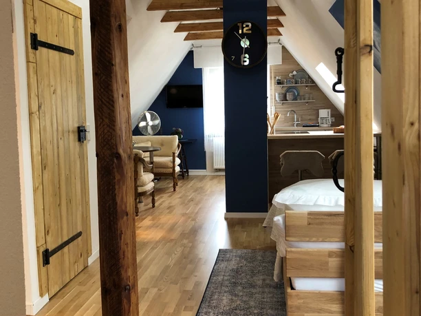 Loft Johanns Hochsitz Charmantes Loft mit Bett, kleiner moderner Küchenecke, Sitzbereich im hinteren Teil, Holzbalken sichtbar im Raum.