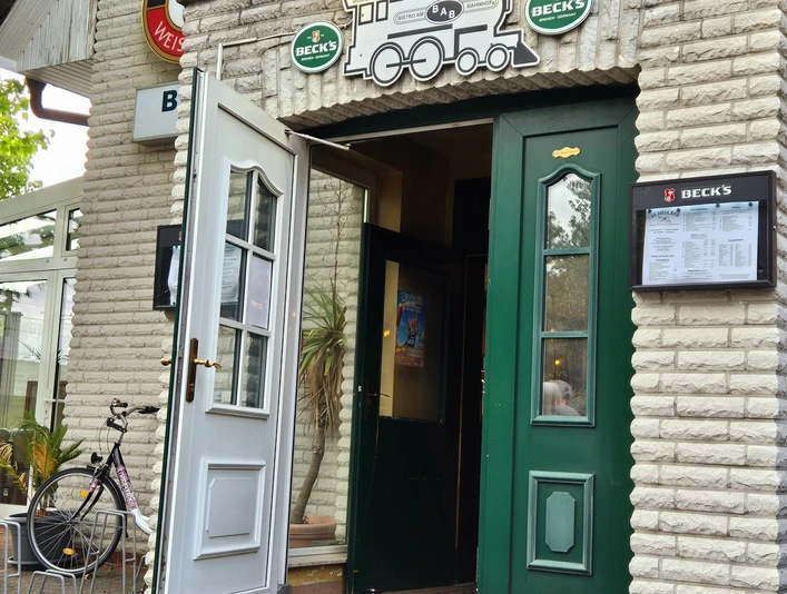 BaB Bistro am Bahnhof Vorderansicht Vorderansicht einer gemauerten Fassade mit grünen Türen und offenem Torbogen unter einem Bierwerbeschild. Ein Fahrrad steht links vom Eingang, signalisiert ein lokal etabliertes Ambiente.