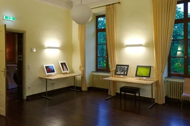 Ausstellungsraum mit zwei Tischen zwischen großen Fenstern, auf denen gerahmte Fotografien stehen .