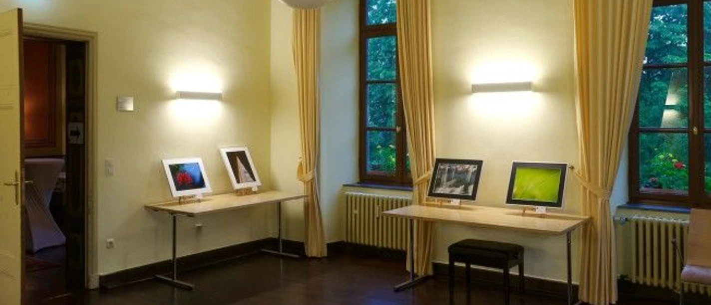 Ausstellungsraum mit zwei Tischen zwischen großen Fenstern, auf denen gerahmte Fotografien stehen .