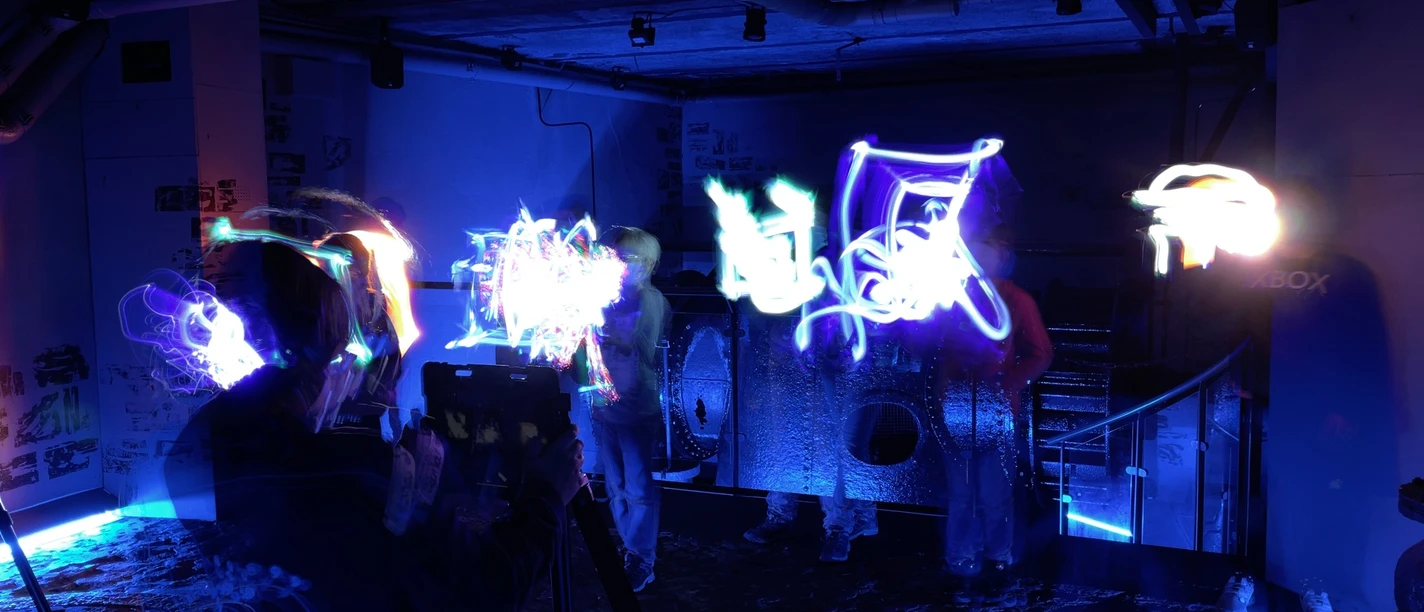 Lightpainting Graffiti Dunkler Raum mit lebendigen, bunten Lichtmalereien vor industrieller Kulisse mit Beton und Metall.