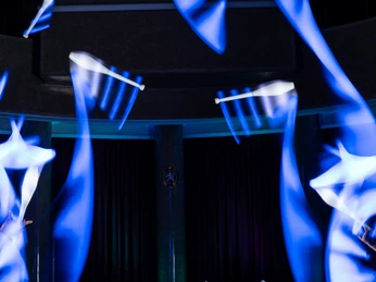 Fusion Showteam 3.jpeg Zwei Artisten jonglieren im Dunkeln mit keulenartigen Requisiten, die in lebhaftem Blau leuchten.