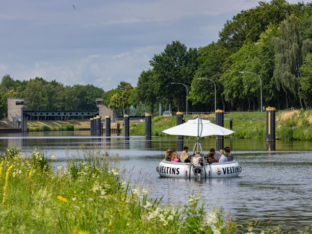 BBQ-Donut Lingen ©Karl-Heinz Berger.jpg Eine Gruppe sitzt auf einem runden BBQ-Boot mit Sonnenschirm auf einem ruhigen Kanal bei Lingen.