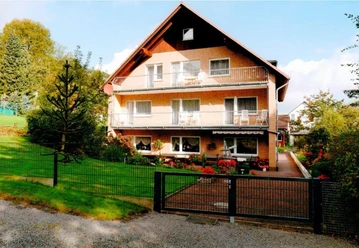 FH Brinks.jpg Drei-stöckiges Ziegelhaus mit Balkon und umgebendem Garten; sonniger Tag mit leichter Bewölkung.