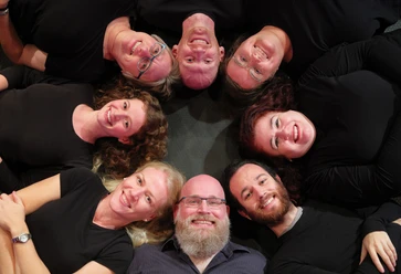Improthesen_Foto_Klawunn_4687a (Flyerfoto).jpg Eine Gruppe von acht Menschen liegt lächelnd in einem Kreis auf dem Boden und blickt zur Kamera.