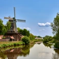 Hengstforder Mühle_Foto Ostfriesland Touristik.jpg Historische Windmühle am Flussufer mit blauer Himmelskulisse und üppigem Grün