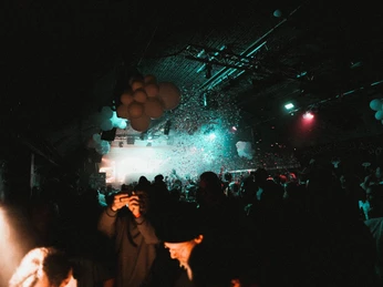 Club Bahnhof Ehrenfeld Eine lebhafte Tanz- und Partyszene in einem dunklen, stimmungsvoll beleuchteten Raum, erfüllt von schwebenden Konfettis und festlichen Luftballons an der Decke.A lively dance and party scene in a dark, atmospherically lit room, filled with floating confetti and festive balloons on the ceiling.