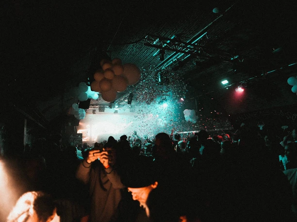 Club Bahnhof Ehrenfeld A lively dance and party scene in a dark, atmospherically lit room, filled with floating confetti and festive balloons on the ceiling.