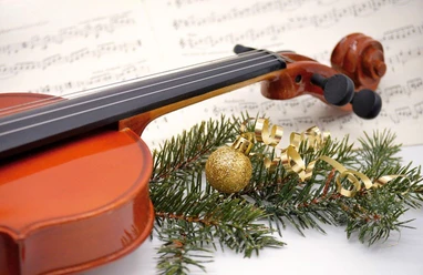 Violine auf Notenblatt mit Tannenzweig, goldener Kugel und festlichem Band