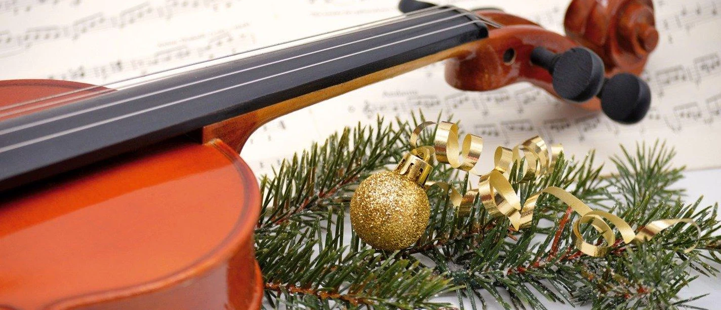 Violine auf Notenblatt mit Tannenzweig, goldener Kugel und festlichem Band